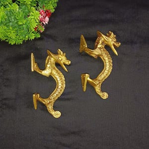 Peut inclure: Deux poignées de porte en forme de dragon dorées avec des détails complexes. Les poignées sont montées sur une surface noire.