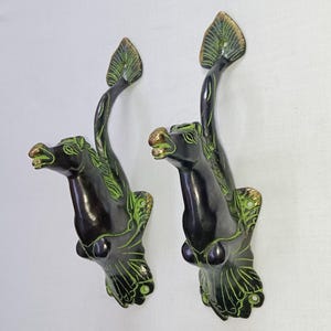 May include: A pair of black and green metal door handles shaped like horses with their heads raised. The handles have a decorative design with green accents.