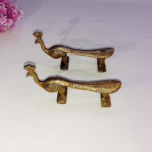 May include: Two ornate brass door handles shaped like peacocks with intricate details. The handles are a rich gold colour and have a traditional design.