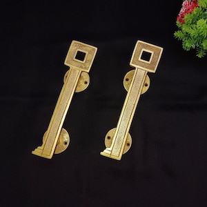 May include: Two gold door handles with a square design and intricate details. The handles are made of solid brass and have a polished finish.