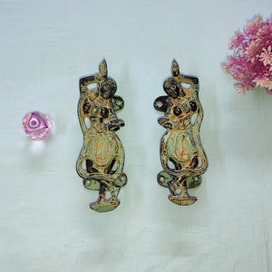 May include: Two matching door handles crafted from dark metal with a weathered green patina finish. Each handle features a detailed relief of a standing figure with arms raised, wearing traditional attire. Both pieces include mounting plates.