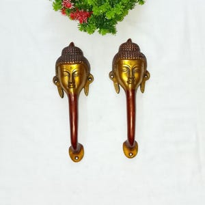 Op de afbeelding: Twee messing Buddha-hoofd deurklinken. De handgrepen hebben een gouden afwerking op het Buddha-hoofd en een donkerbruine handgreep. De handgrepen zijn ongeveer 25 cm lang.