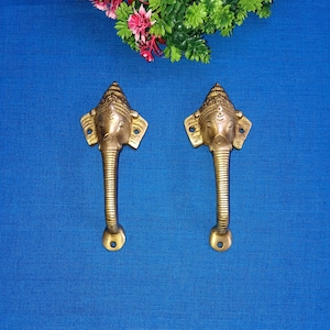 Può includere: Due maniglie per porte dorate a forma di testa di elefante con dettagli intricati. Le maniglie sono su uno sfondo blu.