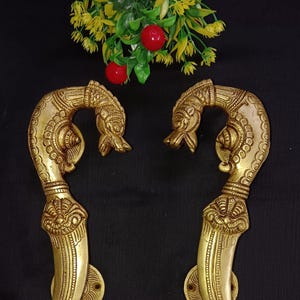 May include: A pair of ornate gold door handles shaped like stylised peacocks with intricate details. The handles are made of brass and have a traditional Indian design.
