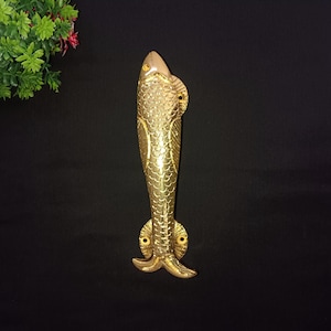 May include: A gold-coloured fish-shaped door handle with a detailed design. The handle is made of metal and has a smooth finish.