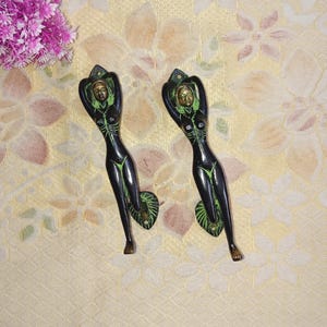 May include: A pair of decorative door handles made of brass. The handles are shaped like a woman with a green and black finish.