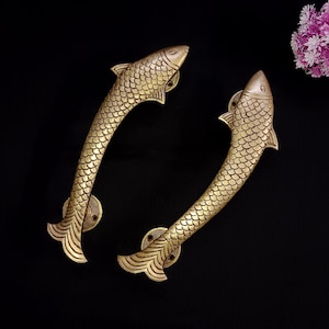 Pode incluir: Duas maçanetas de porta em forma de peixe douradas. As maçanetas são de metal e têm um design detalhado.