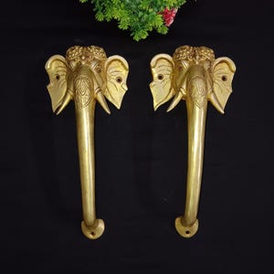 Può includere: Un paio di maniglie per porte dorate a forma di testa di elefante. Le maniglie presentano dettagli intricati e sono in metallo.