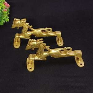 Könnte beinhalten: Zwei goldfarbene Türklinken aus Metall mit einem dekorativen Design eines stilisierten Tierkopfes. Die Griffe sind auf einem rechteckigen Sockel montiert.