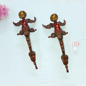 Op de afbeelding: Twee antieke bronzen zeemeerminachtige sculpturen met uitgestrekte armen en gedetailleerde staarten. De figuren hebben een rode romp, een gouden hoofd en bronzen vleugels. De sculpturen zijn decoratief en waarschijnlijk voor interieurontwerp.