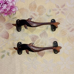 Könnte beinhalten: Zwei schwarze und braune, delphinartige Türklinken mit strukturierter Oberfläche. Die Griffe sind auf einem weißen Hintergrund montiert.