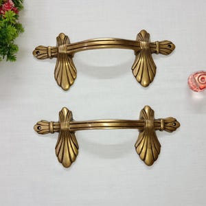 Op de afbeelding: Twee sierlijke goudkleurige deurgrepen met een decoratief waaiervormig ontwerp. De grepen zijn gemaakt van metaal en hebben een gladde, gepolijste afwerking.