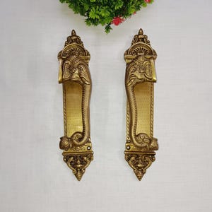 May include: A pair of ornate brass door handles with elephant head designs. The handles are detailed with intricate carvings and have a golden finish.