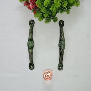 May include: Two antique-style, dark green and bronze door handles with intricate designs. A small, round, copper-colored knob is centered below the handles. Green and red artificial foliage is at the top. These decorative handles are suitable for furniture or doors.