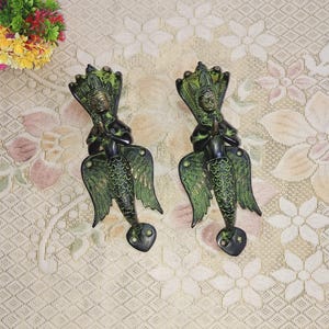 May include: Two ornate brass door handles in the shape of a mythical creature with wings and a human-like face. The handles are green and black with intricate details.