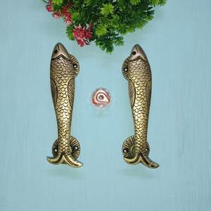 May include: A pair of gold-toned fish-shaped door handles. The handles are detailed with scales and have a smooth, polished finish.