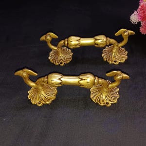 May include: Two gold-toned metal door handles with a decorative peacock design. The handles are ornate and have a detailed design.