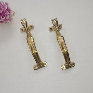 May include: Two gold-toned door handles shaped like horses. The handles are curved and have a detailed design.