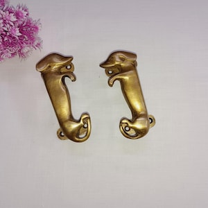 Può includere: Due maniglie per porte a forma di bassotto color oro. Le maniglie sono dettagliate con la testa, le gambe e la coda del bassotto.