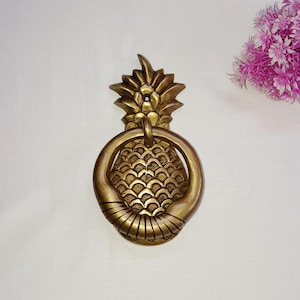 Op de afbeelding: Een gouden deurklopper in de vorm van een ananas met een ringvormige handgreep.