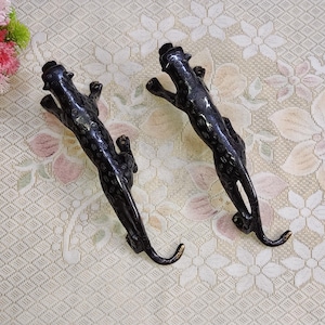 May include: Two black panther figurines with detailed fur patterns. The figurines are made of metal and have a sleek, modern design.