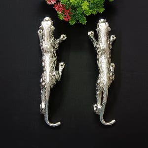 Könnte beinhalten: Zwei silberne Türklinken in Form von Leoparden. Die Griffe sind mit Flecken verziert und haben ein realistisches Aussehen.