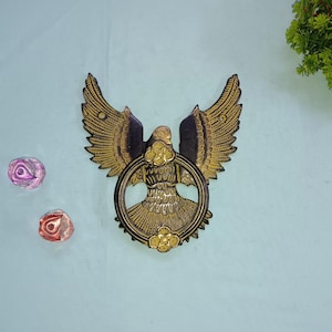 Könnte beinhalten: Ein goldfarbener Adler aus Metall mit ausgebreiteten Flügeln, der einen runden Ring in seinen Krallen hält. Der Adler hat komplizierte Details und einen schwarzen Hintergrund.