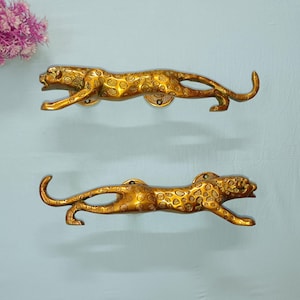 Peut inclure: Deux poignées de porte dorées en forme de léopards. Les poignées sont détaillées avec des taches et ont une apparence réaliste.