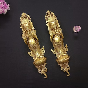May include: Two gold-toned wall-mounted decorative sculptures of the Hindu deity Ganesha. Each sculpture features intricate details and a lotus-shaped base.