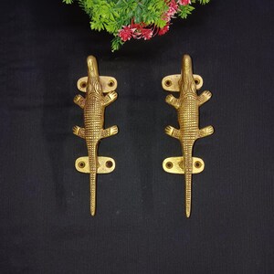 May include: A pair of gold-toned crocodile-shaped door handles. The handles are detailed with textured scales and have a long, slender tail.