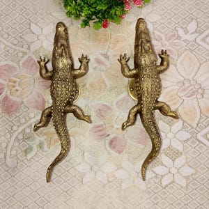 May include: Two gold-colored crocodile door handles. The handles are detailed with scales and have a realistic crocodile design.