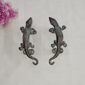 May include: Two antique bronze door handles shaped like lizards with detailed scales and a textured finish.
