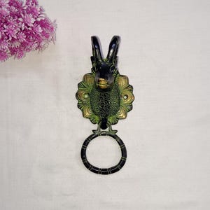 May include: A decorative brass wall hook featuring a deer head design. The hook has a black finish with green and gold accents. The deer head is mounted on a floral-shaped base, and includes a circular ring for hanging items.