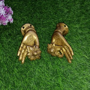 May include: A pair of gold-toned metal door handles shaped like hands holding a flower. The handles are detailed with intricate designs and are perfect for adding a touch of elegance to any home.
