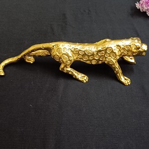 Peut inclure: Une sculpture en métal dorée représentant un léopard accroupi. La sculpture est détaillée avec des taches et a une apparence réaliste.