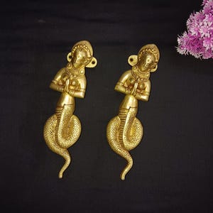 May include: A pair of gold-toned door handles shaped like a woman with a snake tail. The woman is in a prayer position with her hands clasped together in front of her chest.