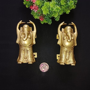Może przedstawiać: Para złotych klamki drzwiowych w kształcie hinduskiego bóstwa Ganesha. Klamki są ozdobione misternymi rzeźbami i mają tradycyjny design.