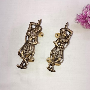 Op de afbeelding: Twee sierlijke messing deurgrepen in de vorm van dansende figuren. De figuren zijn in traditionele Indiase stijl, met ingewikkelde details en vloeiende kleding.