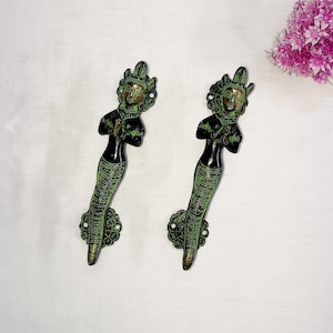 May include: Two ornate green and gold door handles featuring a woman figure design. The handles are made of metal and have a traditional Indian style.