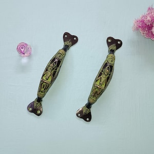 May include: Two ornate brass door handles with a dark brown finish and intricate gold designs. The handles have a heart-shaped top and a curved body.