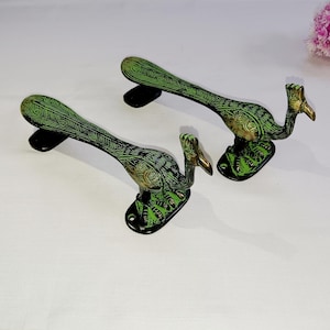 May include: A pair of green peacock-shaped door handles with intricate details. The handles are made of metal and have a polished finish.