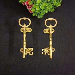 May include: Two gold-toned key-shaped door handles with intricate details. The handles are mounted on a black background.