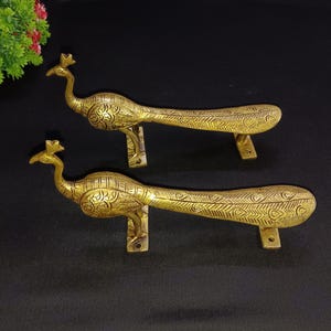 Może przedstawiać: Dwa złote uchwyty do drzwi w kształcie pawia z misternymi detalami. Uchwyty są wykonane z metalu i mają tradycyjny design.