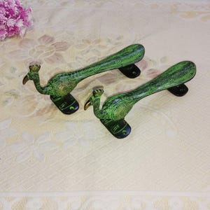 Może przedstawiać: Dwa zielone uchwyty do drzwi w kształcie pawia z misternymi detalami. Uchwyty są wykonane z metalu i mają czarne wykończenie.