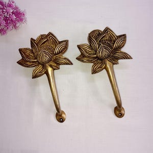 May include: Two gold-toned metal lotus flower door handles with a detailed design. The handles are attached to a wall.