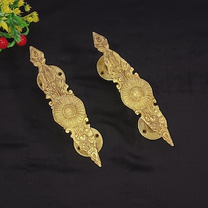 May include: A pair of ornate gold door handles with intricate floral designs. The handles are long and narrow with a pointed tip at the end.