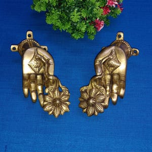 Puede incluir: Un par de tiradores de puerta de latón en forma de manos que sostienen flores. Los tiradores son de color dorado y tienen detalles intrincados.