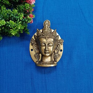 Op de afbeelding: Een messing deurklopper met een gedetailleerd ontwerp van een vrouwengezicht met gesloten ogen en een kroon. De deurklopper is rond en heeft een decoratieve rand.