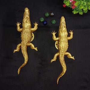 May include: Two gold crocodile door handles. The handles are detailed with textured scales and have a realistic crocodile design.