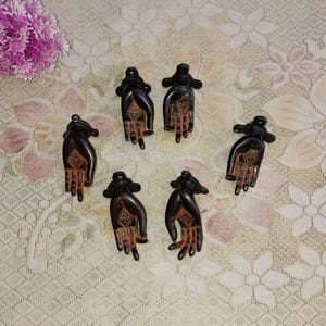 Op de afbeelding: Zes zwarte metalen handvormige deurknopjes met ingewikkelde ontwerpen. De knoppen zijn gerangschikt in twee rijen van drie.